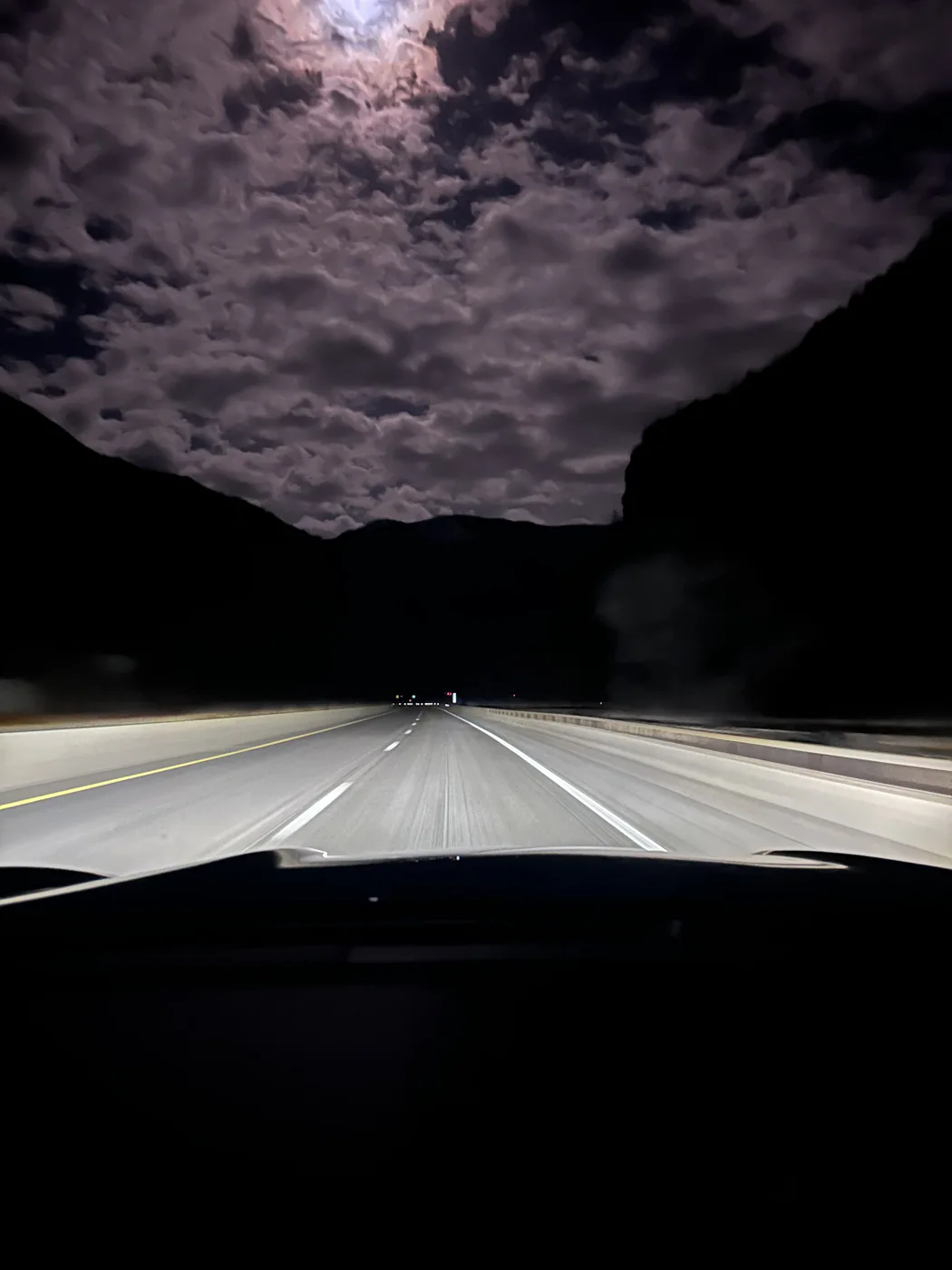 An open road at night beneath moonlit clouds