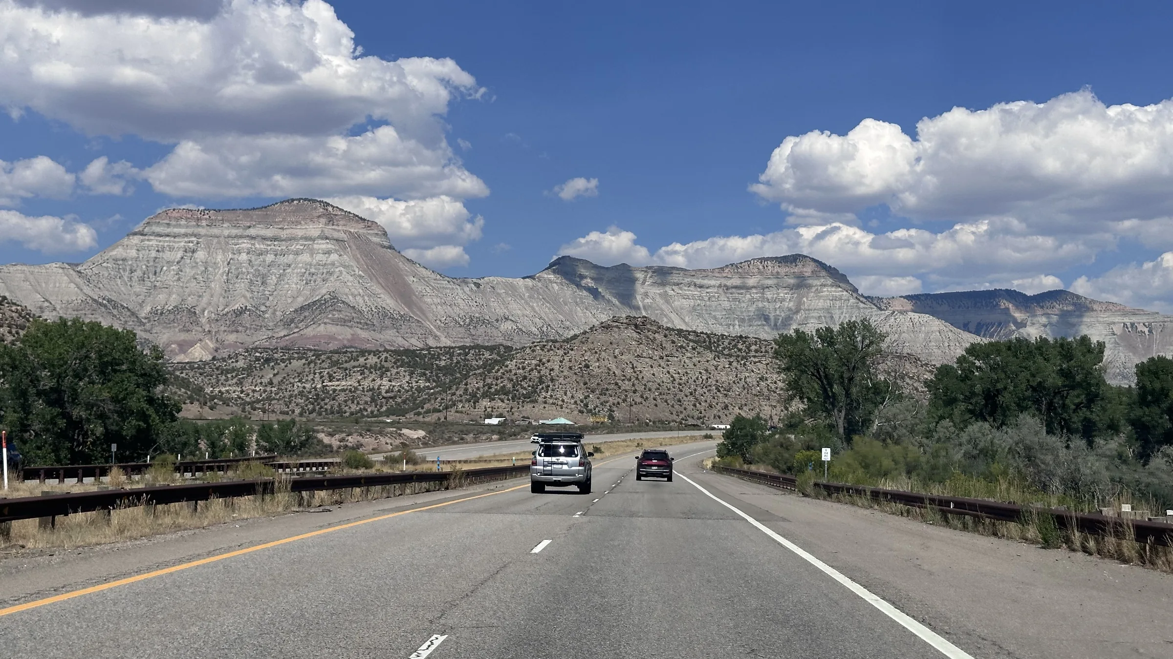 A highway curves toward layered Western mountains beneath a blue sky